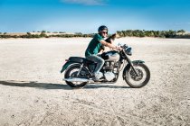 Mid adult man and dog riding motorcycle on arid plain, Cagliari, Sardinia, Italy — Stock Photo