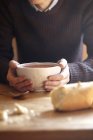 Jovem na mesa da cozinha com as mãos segurando tigela de sopa — Fotografia de Stock