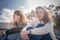 Дві похмурі молоді друзі-жінки сидять на вітряному пляжі — стокове фото