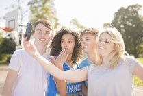 Cuatro jugadores de baloncesto adultos jóvenes tomando selfie smartphone en la cancha - foto de stock