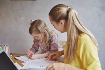 Мать учит дочь писать за столом — стоковое фото