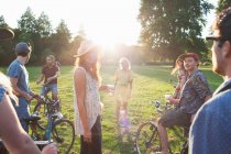 Group of party going adults arriving in park on bicycles at sunset — Stock Photo