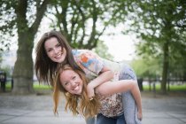 Porträt von zwei jungen besten Freundinnen, die Huckepack im Park zurückgeben — Stockfoto