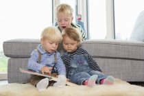 Boy and two toddlers reading childrens book on living room floor — Stock Photo