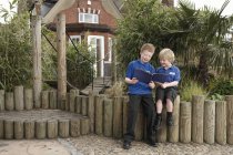Двое школьников читают книгу на бревенчатом заборе — стоковое фото