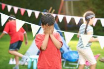 Boy covering his eyes for hide and seek with brother and sister in garden — Stock Photo