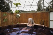 Зріла жінка розслабляється в гарячій ванні в еко-відступ — стокове фото