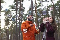 Jovem casal soprando bolhas na floresta — Fotografia de Stock