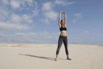 Mulher adulta média exercitando-se com os braços levantados na praia — Fotografia de Stock