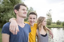 Grupo de jóvenes adultos, de pie junto al lago, sonriendo - foto de stock