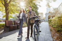 Casual businessman and woman pushing bike through park — Stock Photo
