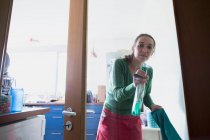 Вид через стеклянную дверь средней взрослой женщины, брызгающей чистящим средством — стоковое фото