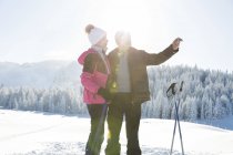 Un couple d'aînés sur un paysage enneigé à l'aide d'un smartphone pour prendre une photo, Sattelbergalm, Tyrol, Autriche — Photo de stock