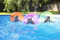 Tres niños compitiendo en anillos inflables en piscina de jardín - foto de stock