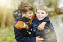 Hermanos pre-adolescentes en chaquetas abrazándose al aire libre - foto de stock