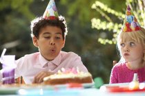 Garçon soufflant des bougies sur gâteau d'anniversaire à la fête d'anniversaire de jardin — Photo de stock