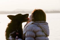 Dog licking mid adult womans face on lakeside — Stock Photo