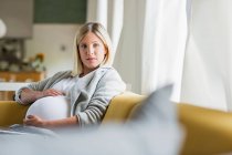 Embarazo a término mujer joven sosteniendo el estómago en sofá - foto de stock
