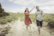 Happy young couple running barefoot along sandy track, Cody, Wyoming, USA — Stock Photo