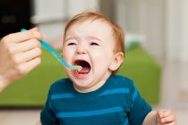 Crying baby sitting in chair being fed — Stock Photo