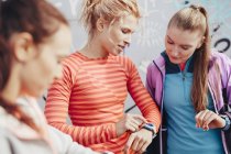 Três corredoras femininas verificando o tempo no smartwatch — Fotografia de Stock