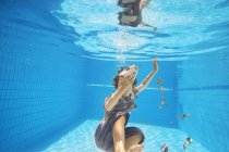 Underwater view of boy in swimming pool grabbing euro notes and coins — Stock Photo