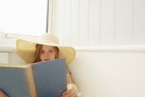 Chica en la lectura del sombrero de sol en el porche del apartamento de vacaciones - foto de stock