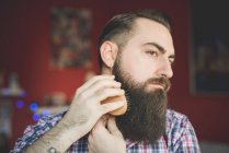 Joven barbudo cepillándose la barba - foto de stock