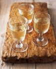 Glasses of white wine on wooden cutting board — Stock Photo