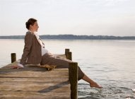 Женщина сидит на пирсе у озера — стоковое фото