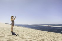 Mujer joven fotografiando mar con smartphone, Dune de Pilat, Francia - foto de stock