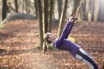 Side view of young woman in forest leaning back using resistance bands, looking up — Stock Photo