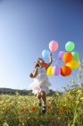 Menina pulando de alegria com balões coloridos no prado de flores silvestres, Maiorca, Espanha — Fotografia de Stock