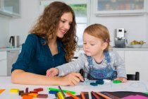 Teenage girl and female toddler drawing at kitchen table — Stock Photo