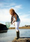 Young girl looking in net at rock pool — Stock Photo