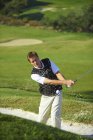 Golfista tomando swing de golf en trampa de arena, pelota de golf en el aire - foto de stock