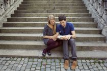 Young couple sitting on old street stairway reading newspaper — Stock Photo