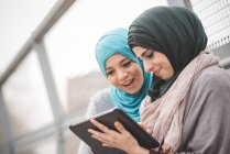Two young women wearing hijabs using digital tablet on footbridge — Stock Photo