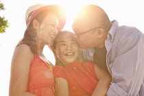 Parents kissing daughter on cheek in sunlight — Stock Photo