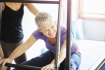 Mujer madura y tutor practicando pilates en mesa trapecio en el gimnasio pilates - foto de stock