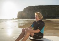 Senior woman surfer sitting on surfboard, Camaret-sur-mer, Brittany, France — Stock Photo