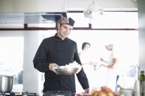 Chef macho llevando sartén en cocina comercial - foto de stock