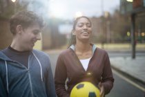 Young man and woman walking in street, holding football — Stock Photo