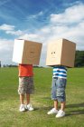 Boys with boxes over heads in rural field — Stock Photo
