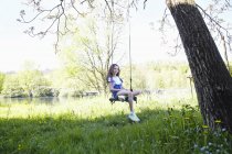 Дівчина сидить на гойдалках в зеленому літньому саду, портрет — стокове фото