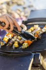 Young mans hand using tongs to turn sausages and kebabs on barbecue griddle — Stock Photo