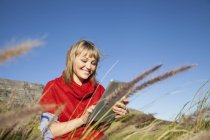 Young woman sitting in long grass using touch screen on digital tablet — Stock Photo