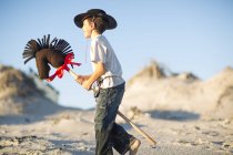 Boy with hobby horse dressed as cowboy in sand dunes — Stock Photo