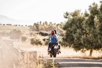 Vista trasera de la pareja que monta la motocicleta en la carretera rural polvorienta, Cagliari, Cerdeña, Italia - foto de stock