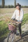 Young woman carrying bunch of sticks on bicycle — Stock Photo